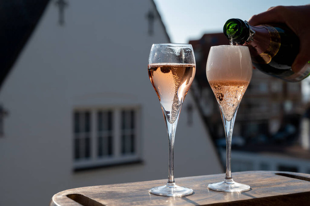 Pouring of rose champagne sparkling wine in flute glasses on outdoor terrace in France in sunny day - Photo, Image