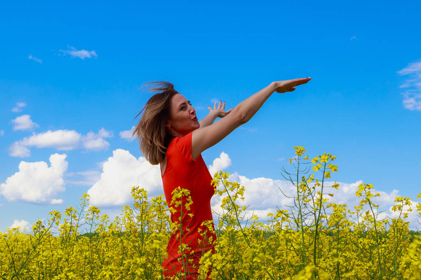 Young pretty woman in colored dress on lightning cheerful yellow background of blooming rapeseed field. The concept of unity with nature - Foto, afbeelding