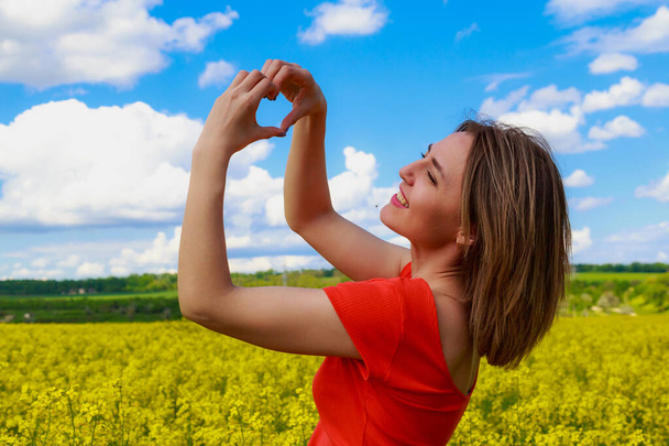 Young pretty woman in colored dress on lightning cheerful yellow background of blooming rapeseed field. The concept of unity with nature - Foto, afbeelding