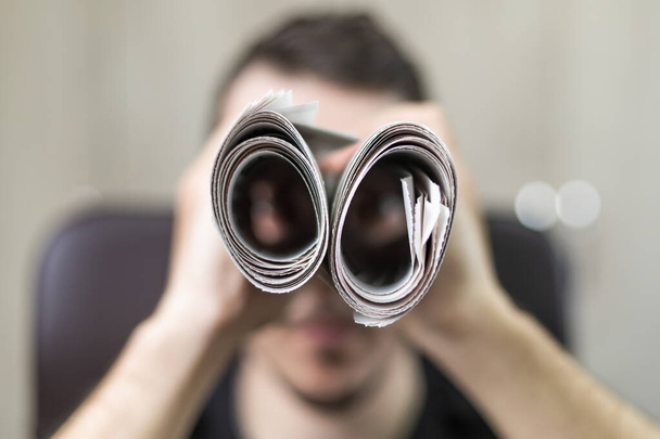 Man holding two twisted roll newspaper. Metaphor or allegory with binoculars. Selective focus on newspapers. Truth search concept - Foto, Imagem