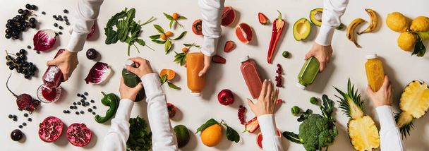 Flat-lay van menselijke handen met verse sappen flessen tussen fruit, bessen, groenten over witte achtergrond, bovenaanzicht. Detox-programma, gezond, schoon eten, veganistisch, fructoriaans dieet, gewichtsverlies concept - Foto, afbeelding