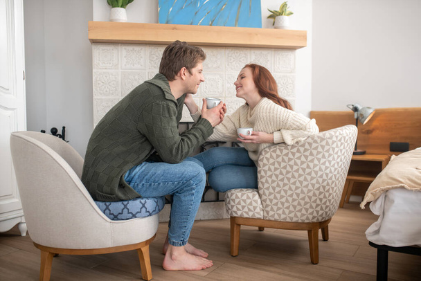 Smiling man and touching woman drinking coffee near fireplace - Photo, image
