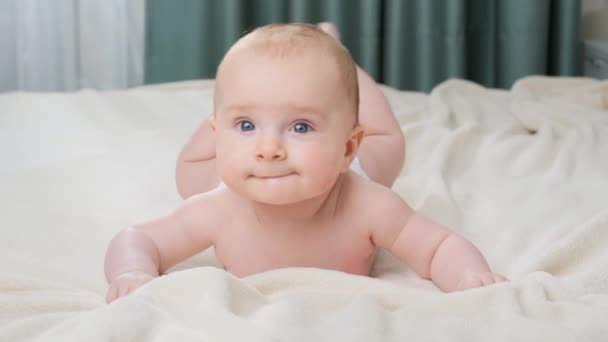 Portret van schattig klein jongetje met blauwe ogen liggend op bed en kijkend in camera. - Video