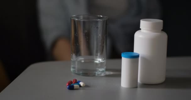 Sklenice vody a nějaké pilulky na stole zblízka na pozadí ženy. Zpomalený pohyb - Záběry, video