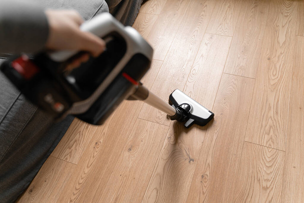 Cleaning wooden floor with wireless vacuum cleaner. Handheld cordless cleaner. Household appliance. Housework modern equipment - Foto, afbeelding