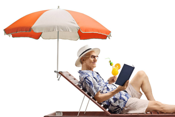 Elderly man enjoying on a sunbed with a book and a cocktail isolated on white background - Photo, Image