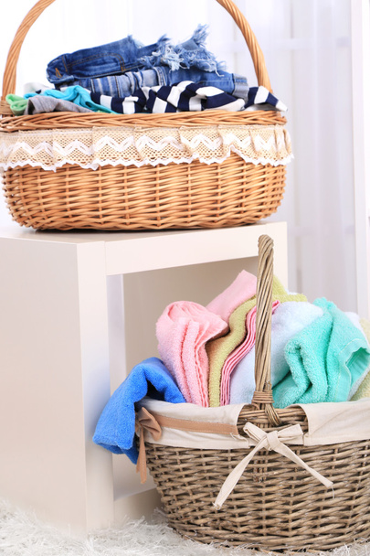 Colorful towels and clothes in baskets on table, on interior background - Фото, изображение