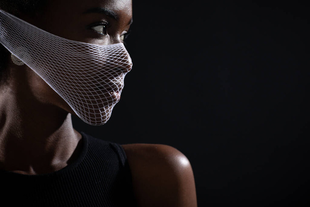 Closeup portrait of african american woman fashion model wearing quarantine medical face mask coarse mesh net on black background. Covid-19 coronavirus protection concept. - Fotoğraf, Görsel