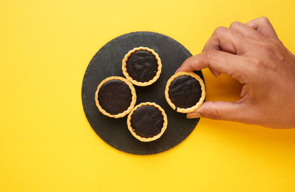 A picture of hand taking chocolate tart on slate plate and yellow background - Photo, Image