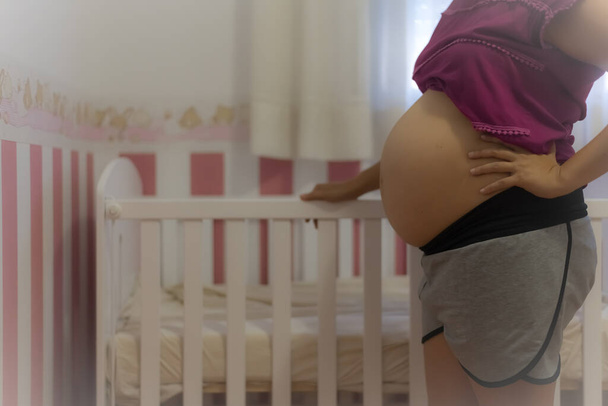 Pregnant woman showing her belly from the side holding a baby crib. Concept, waiting for the newborn - Foto, afbeelding