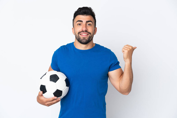 Fešák mladý fotbalista muž přes izolovanou zeď ukazuje na stranu prezentovat produkt - Fotografie, Obrázek