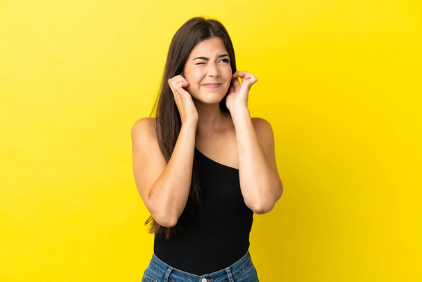 Young Brazilian woman isolated on yellow background frustrated and covering ears - Photo, Image