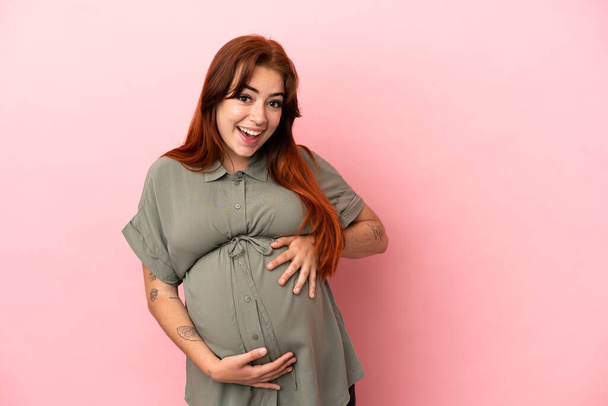 Jovem ruiva caucasiana mulher isolada no fundo rosa grávida e fazendo gesto surpresa - Foto, Imagem