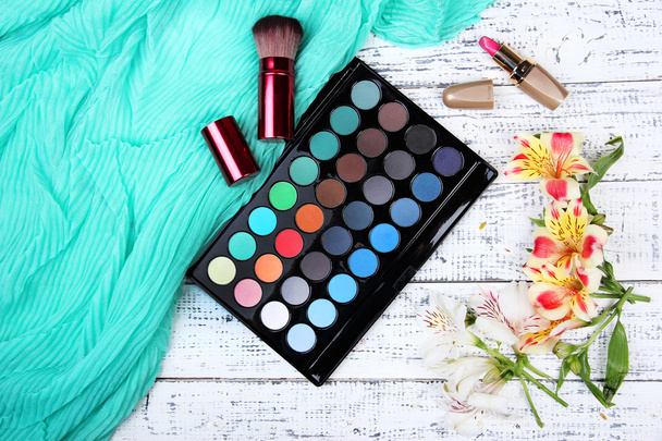 oogschaduw, penseel, lippenstift en bloemen op een houten achtergrond kleur - Foto, afbeelding