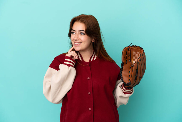 Nuori punapää nainen pelaa baseball eristetty sinisellä taustalla ajattelu idea etsiessään ylös - Valokuva, kuva