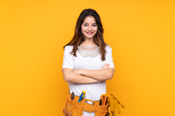Sarı arka planda izole edilmiş genç elektrikçi kadın gülüyor. - Fotoğraf, Görsel