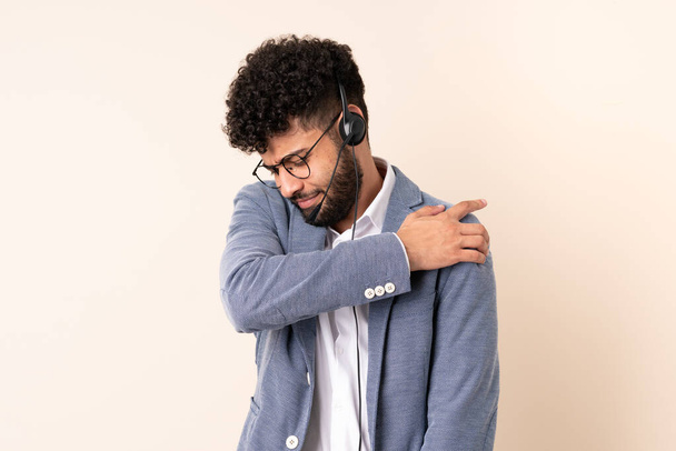 Telemarketer Moroccan man working with a headset isolated on beige background suffering from pain in shoulder for having made an effort - Foto, Imagem