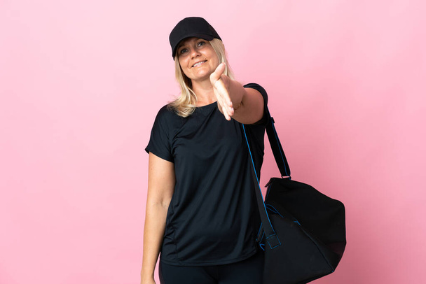 Middle age woman with sport bag isolated on pink background shaking hands for closing a good deal - Valokuva, kuva