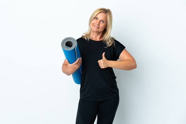 Middle age woman going to yoga classes while holding a mat isolated on white background with thumbs up because something good has happened - Fotoğraf, Görsel