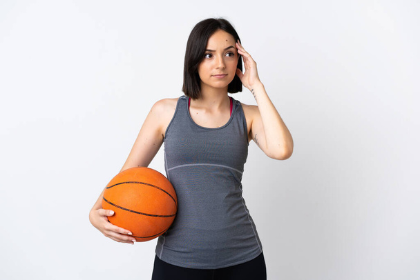 jonge vrouw spelen basketbal geïsoleerd op witte achtergrond met twijfels en denken - Foto, afbeelding