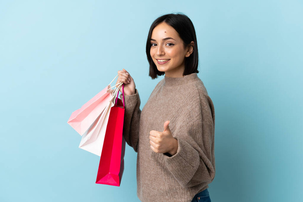 Young caucasian woman isolated on blue background holding shopping bags and with thumb up - Foto, Imagen