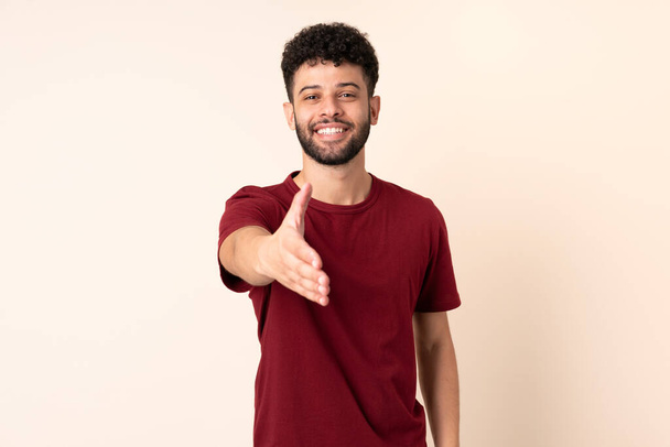 Young Moroccan man isolated on beige background shaking hands for closing a good deal - Photo, Image