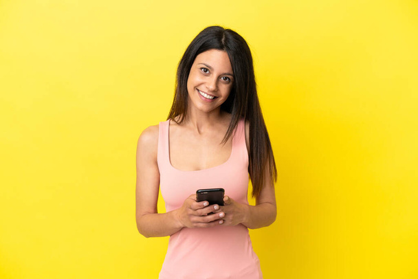 Young caucasian woman isolated on yellow background sending a message with the mobile - Photo, Image