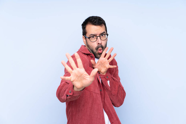 Young caucasian man wearing corduroy jacket over blue background nervous stretching hands to the front - Foto, Imagem