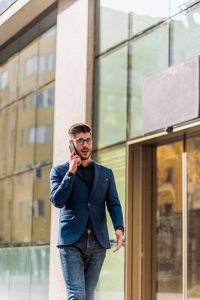 Glücklicher erfolgreicher junger Geschäftsmann mit seinem Handy in der Nähe von Bürogebäuden - Foto, Bild