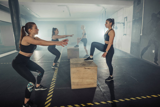 Groep van atletische jonge fit meisjes in sportkleding doen hurken, met een intense benen workout - Foto, afbeelding