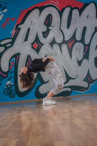 Ελκυστική νεαρή γυναίκα κάνει breakdance κίνηση πάνω από το φόντο γκράφιτι - Φωτογραφία, εικόνα