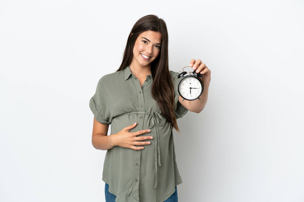 Mujer brasileña joven aislada sobre fondo blanco embarazada y sosteniendo reloj - Foto, Imagen