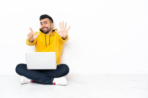 Caucásico hombre sentado en el suelo con su portátil contando siete con los dedos - Foto, imagen