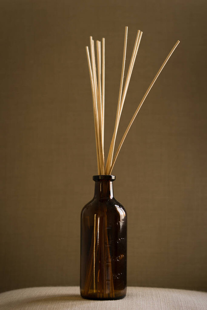 A dark glass diffuser bottle with natural reed sticks put on a pillow - Foto, Bild