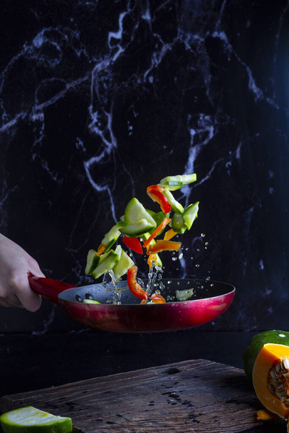 A vertical closeup shot of sliced vegetables flying from a pan during mixing - 写真・画像
