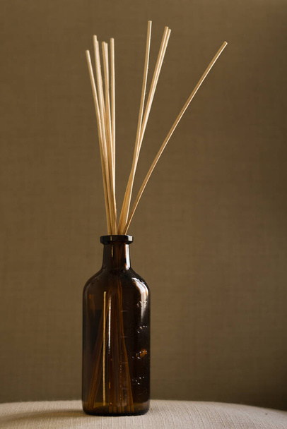 A dark glass diffuser bottle with natural reed sticks put on a pillow - Foto, imagen