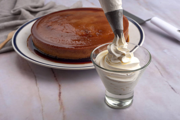 A closeup shot of whipping cream in a glass next to a cake - Фото, зображення