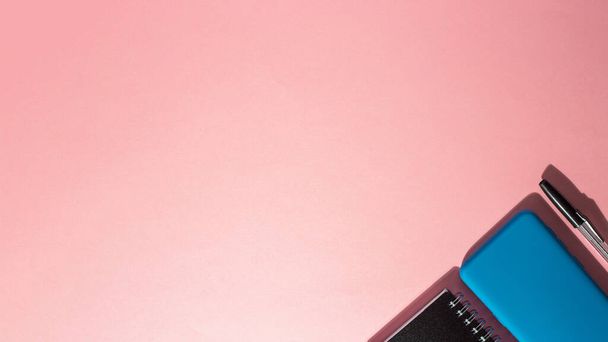 A top view of a smartphone and a notepad with a pen on a pink background - Valokuva, kuva