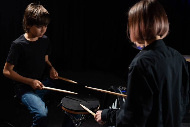 Young caucasian woman teaches a boy to play the drums in the studio on a black background. Music school student - Фото, изображение