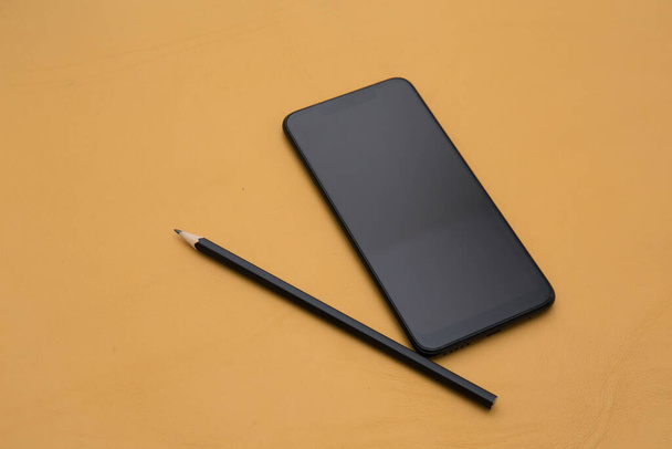 Photo of smartphone with white screen and pencil on yellow leather background - Фото, зображення