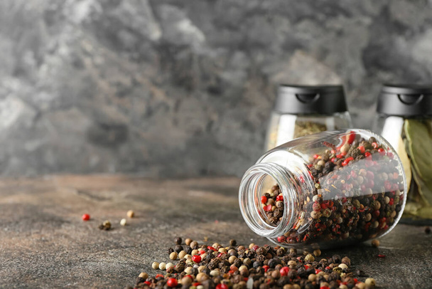 Tarro volcado con granos de pimienta mezclados sobre fondo grunge - Foto, imagen