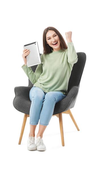 Happy young woman with tablet computer sitting in armchair on white background - Photo, Image
