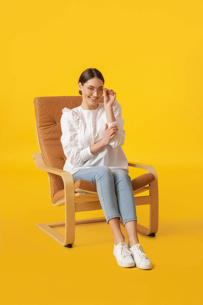 Mujer joven sentada en sillón sobre fondo de color - Foto, imagen