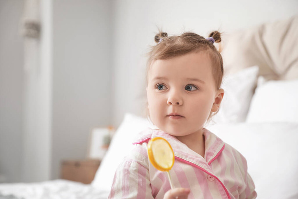 Cute little girl with lollipop in bedroom, closeup - Fotografie, Obrázek