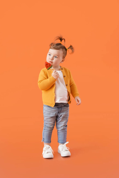 Cute little girl eating lollipop on color background - Fotó, kép