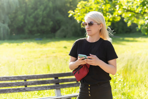 Nuori nainen käyttää älypuhelinta puistossa. - Valokuva, kuva