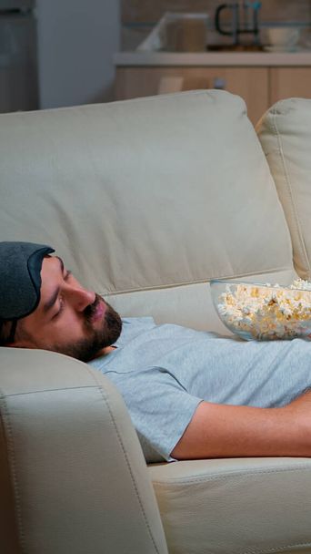 Mann schließt Augen und schläft auf der Couch im Wohnzimmer ein - Foto, Bild