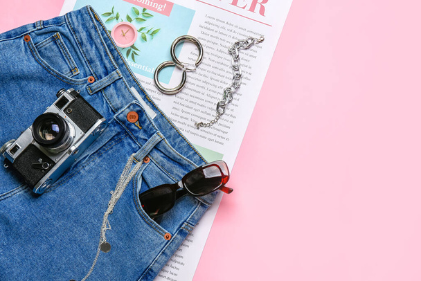 Stylish female accessories with jeans pants, newspaper and photo camera on color background - Photo, Image
