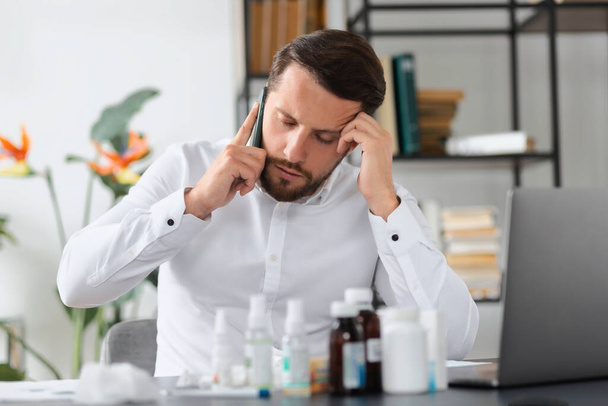 Young responsible employee male or businessman sick for influenza infection works while sitting in the office, virus, cold, feeling unwell concept - Photo, Image