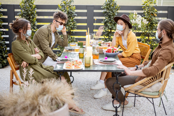 Amici tristi in maschera viso cenare insieme nel cortile all'aperto - Foto, immagini